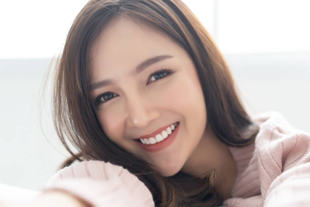 Closeup portrait of inspired caucasian Asian lady wearing knitted sweater pink cold smilling and taking selfie at her home.Concept woman lifestyle and winter. Model fashion shooting. Autumn, winter season.
